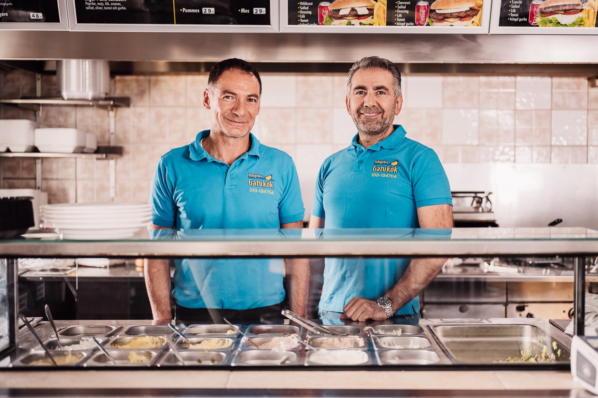 Young confident owner of street food truck holding hotdogs against her colleague